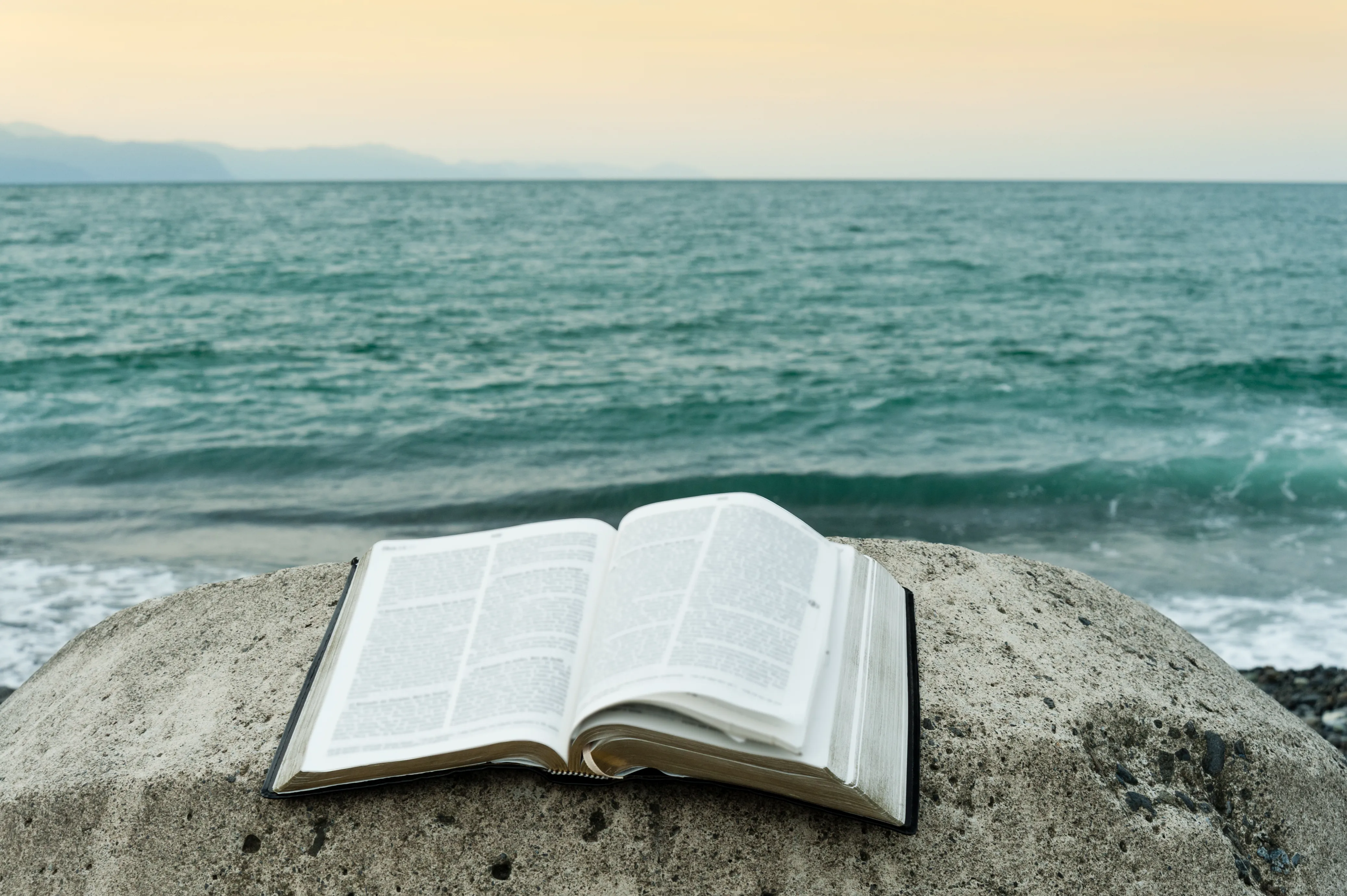 An open Bible on a rock beside the sea